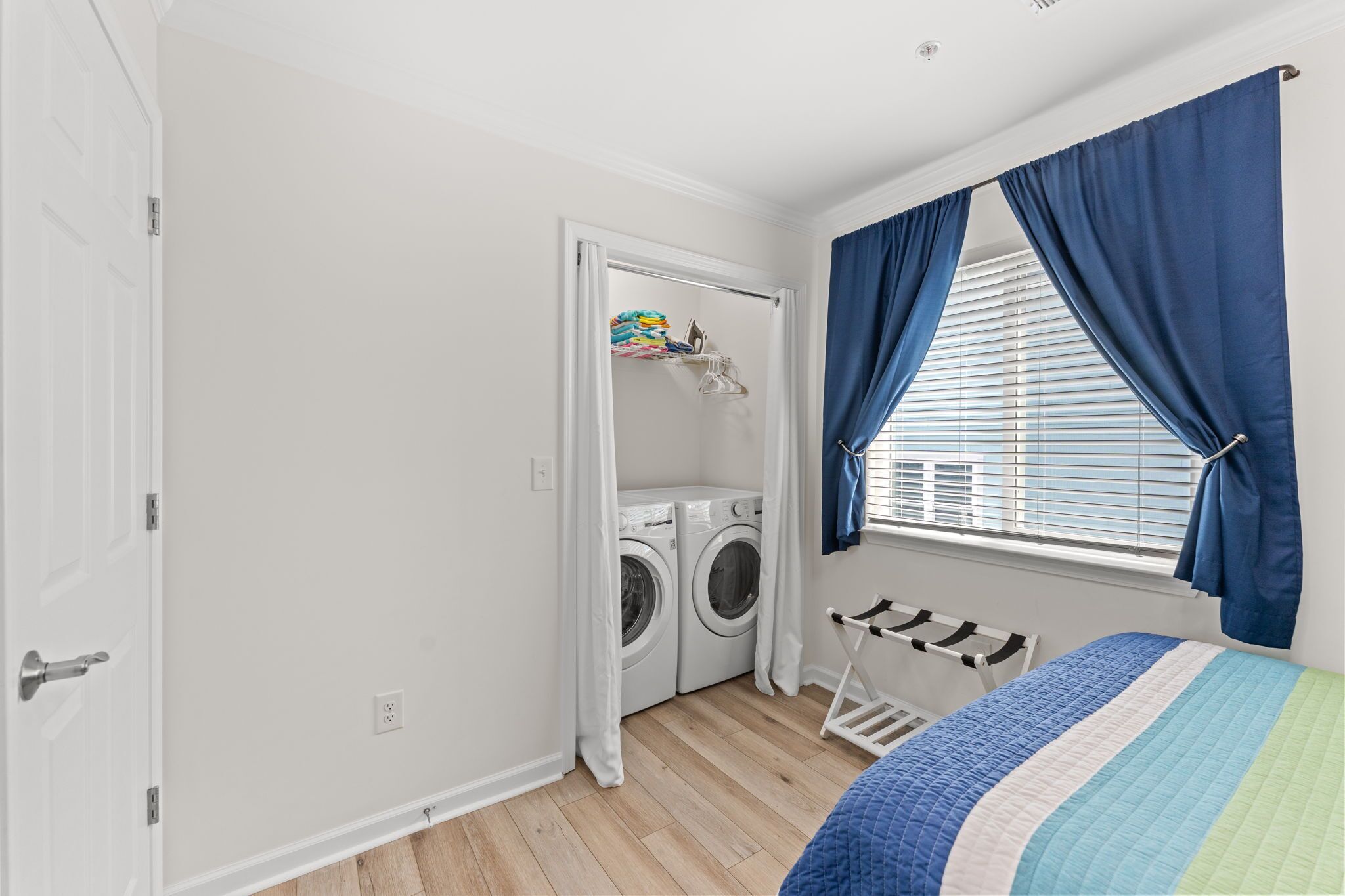 Une chambre à coucher avec un lit, une fenêtre avec des rideaux, un lave-linge et un étendoir.