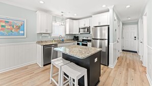 Una cocina moderna con armarios blancos, electrodomésticos de acero inoxidable, una encimera de granito y un mapa en la pared.
