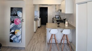 A modern kitchen with a central island, two bar stools, and a refrigerator.