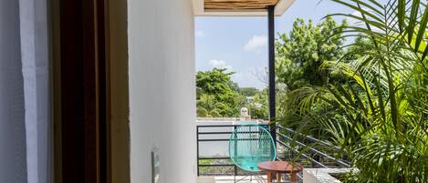 Un balcón con vistas a la vegetación, una silla de metal, una mesa y un techo de madera.
