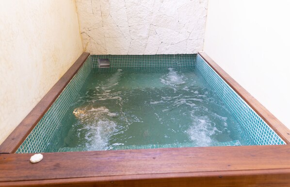 A wooden bathtub with a green tiled interior, set against a textured wall. - La Galuna Bacalar (Bacalar)