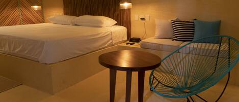 Ein Hotelzimmer mit Bett, einem kleinen Tisch, einem Sessel und einem Nachttisch mit Lampe.