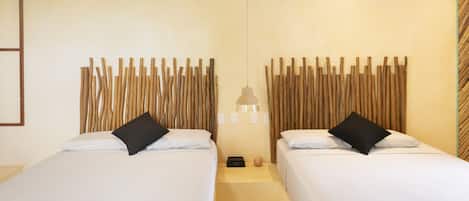 Habitación de hotel con dos camas, cada una con ropa blanca y almohadas negras, cabecero de madera, mesita de noche pequeña con lámpara y unidad de aire acondicionado en la pared.