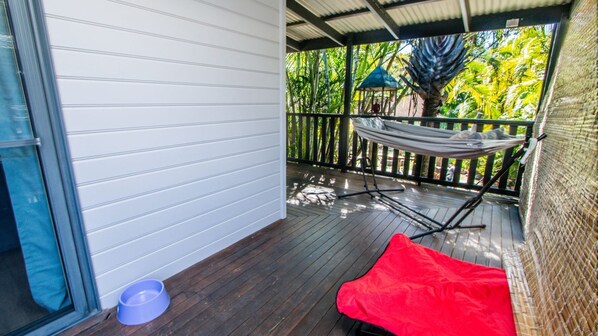 A covered outdoor area with a hammock, a red cushion, and a blue bowl on the floor.