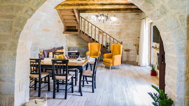 Un coin repas avec un mur en pierre, un escalier en bois et des chaises jaunes.