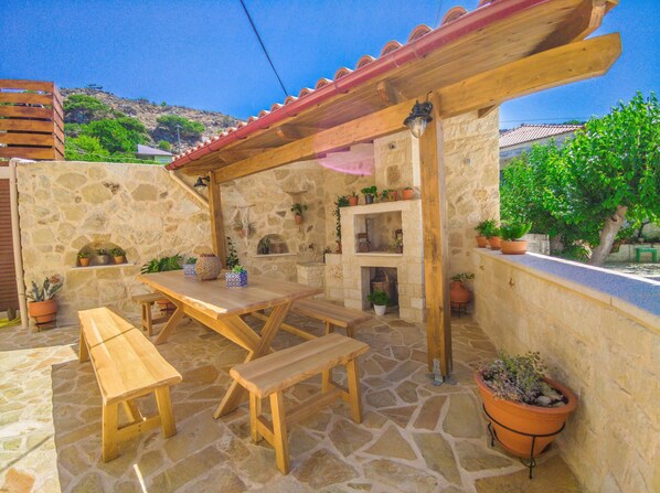 Une terrasse en pierre avec des meubles en bois, une pergola et des plantes en pot.