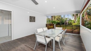 Een moderne patio met een glazen tafel en stoelen, omgeven door een houten terras en uitzicht op tropische begroeiing.