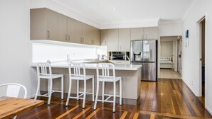 Een moderne keuken met een centraal eiland, witte barkrukken, roestvrijstalen apparatuur en een houten vloer.