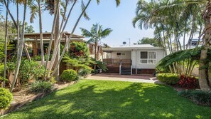 Une maison de plain-pied dotée d’un porche abrité, entourée d’une végétation tropicale luxuriante.