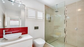 Une salle de bain moderne avec une douche à l’italienne en verre, un lavabo blanc et un mur d’accent rouge.