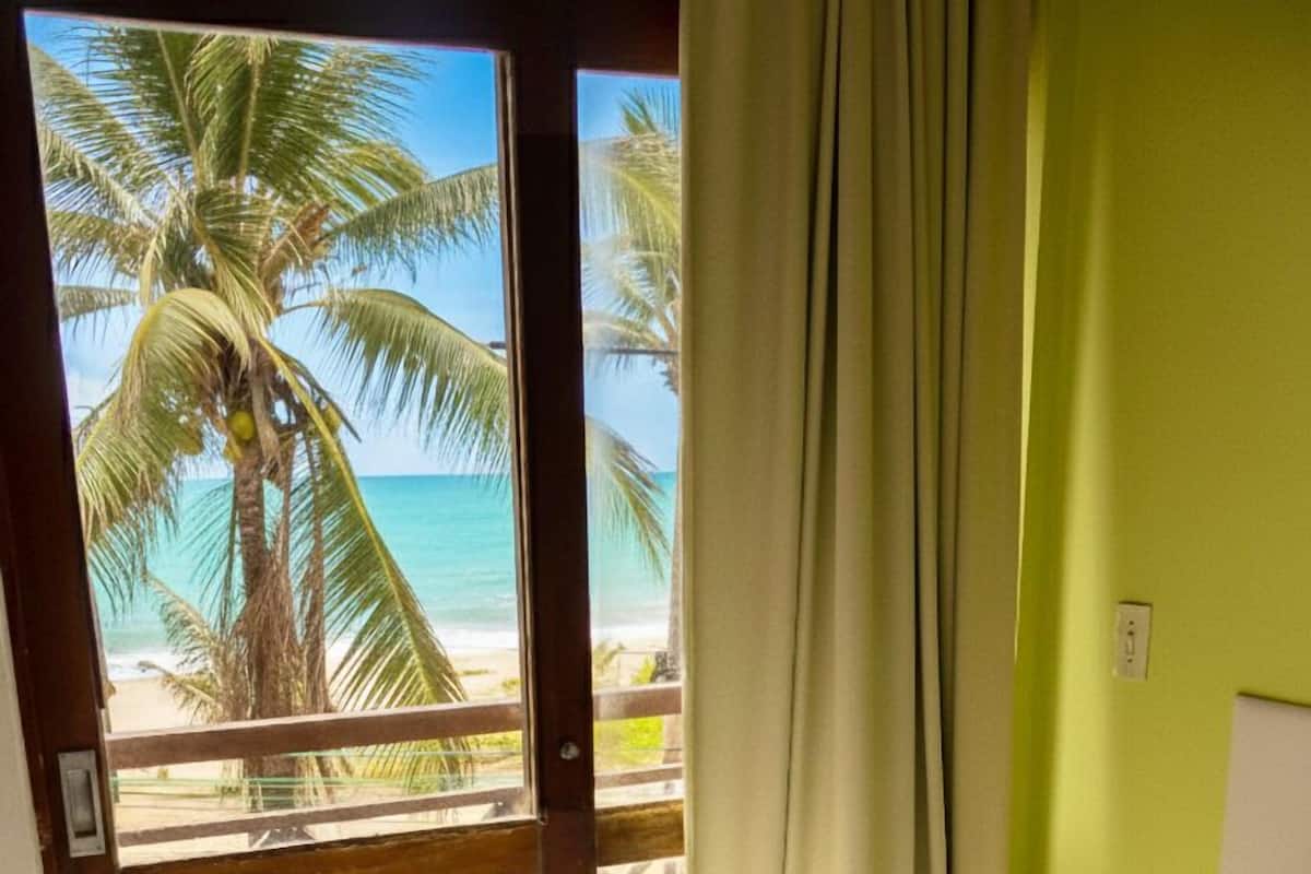 Quarto com cama, vista para a praia e cortina.