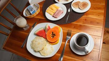 Una mesa de madera con alimentos para el desayuno, incluyendo tostadas, jamón, queso y fruta.
