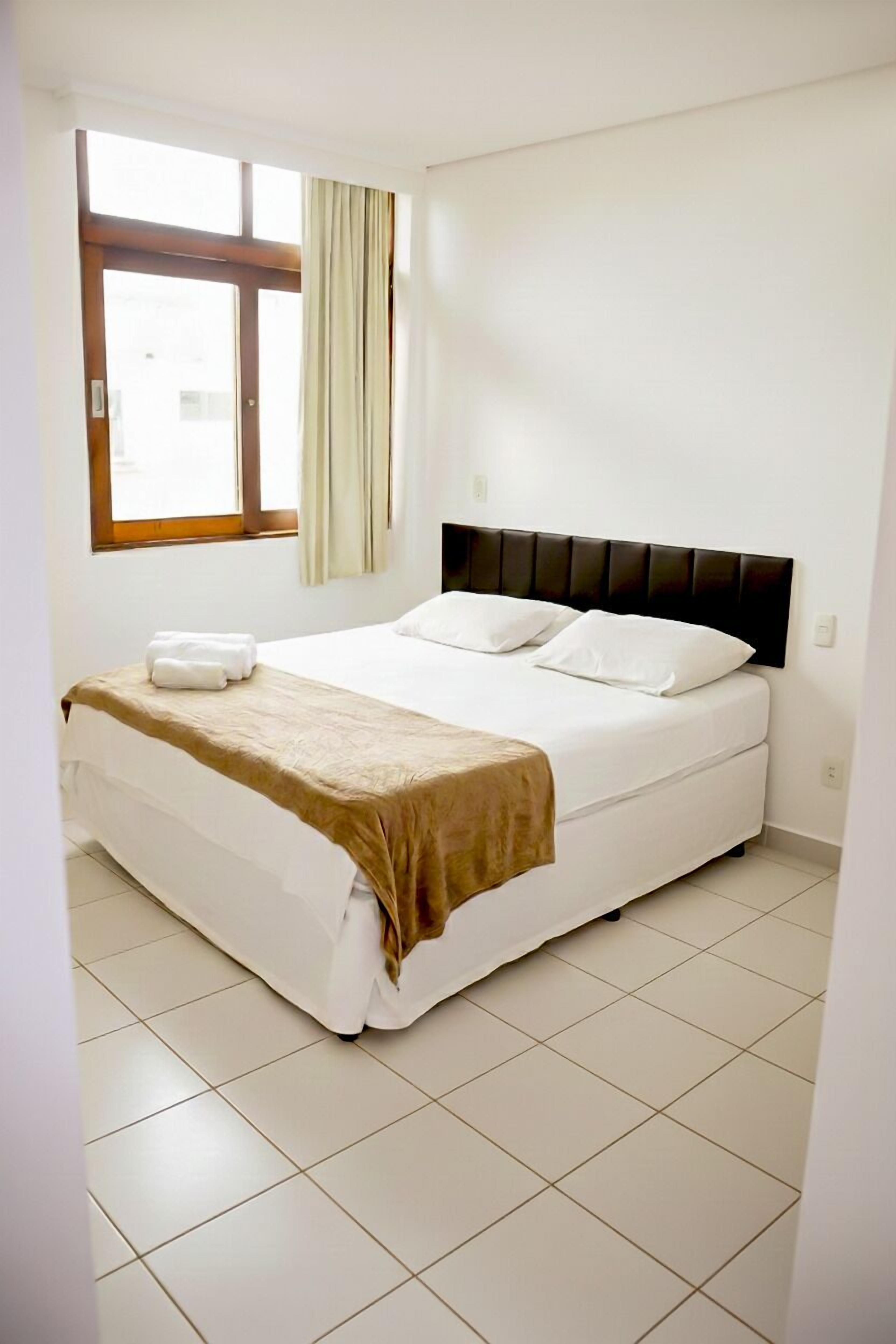 Une chambre d’hôtel avec un lit, une fenêtre avec des rideaux et un sol carrelé.