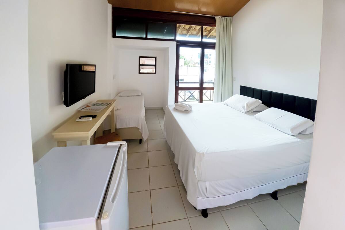 Quarto de hotel com uma cama, uma secretária, uma televisão e uma janela.