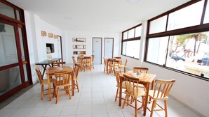 Un vaste espace dédié à la salle à manger, avec de nombreuses tables et chaises en bois, de grandes fenêtres donnant sur la rue et un sol carrelé impeccable.