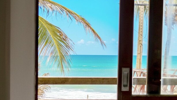 Une chambre avec vue sur la plage, une balustrade en bois et un lit avec des serviettes pliées.