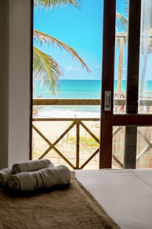 Une chambre avec vue sur la plage, une balustrade en bois et un lit avec des serviettes pliées.