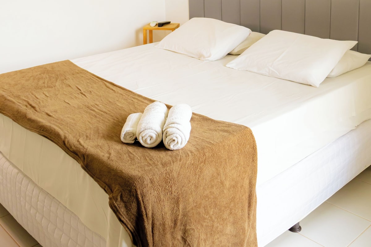 Quarto de hotel com uma cama, um cobertor marrom e um ar condicionado fixado na parede.