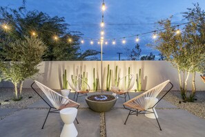 Een terras buiten met een vuurkuil, lichtjes en cactussen.