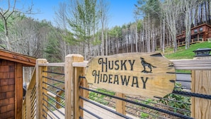 Puinen kyltti, jossa on kuva huskystä ja teksti ”Husky Hideaway”, puisen aidan sisäänkäynnin kohdalla.
