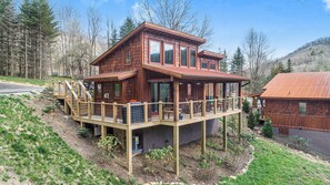 A wooden cabin with a deck, large windows, and a stone foundation. - Husky Hideaway - Mountain views, Pet-friendly, Wi-Fi, and King Bed. (Banner Elk)