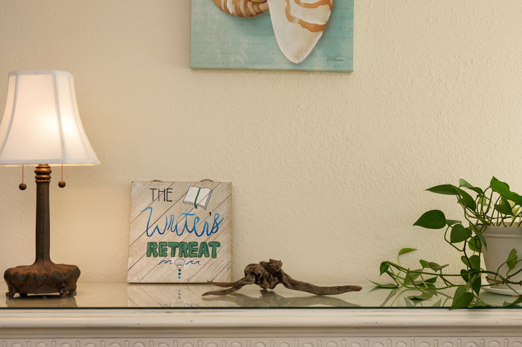 A lamp, a framed sign reading "The Writer's Retreat," and a plant on a mantelpiece.