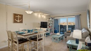 A dining area with a table set for four, a television, and a view of the outdoors. - First Floor, directly on the Ocean & Well Stocked Condo! Listen to Waves Crash! (Nags Head)