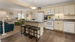 A modern kitchen with white cabinets, a central island with stools, a microwave, and a stove. - First Floor, directly on the Ocean & Well Stocked Condo! Listen to Waves Crash! (Nags Head)