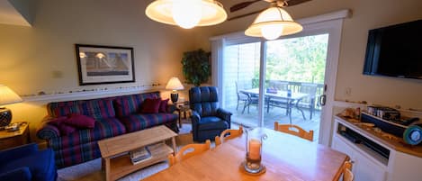A cozy living room with a sofa, a chair, a wooden table, and a TV mounted on the wall.