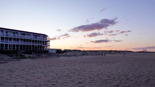 A beachfront hotel with multiple balconies, sandy beach in the foreground, and a clear sky with clouds. - Ocean Block. Steps from the beach! (Bethany Beach)