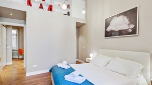 A modern hotel room with a large bed, a blue accent wall, a white headboard, and a framed floral artwork on the wall.