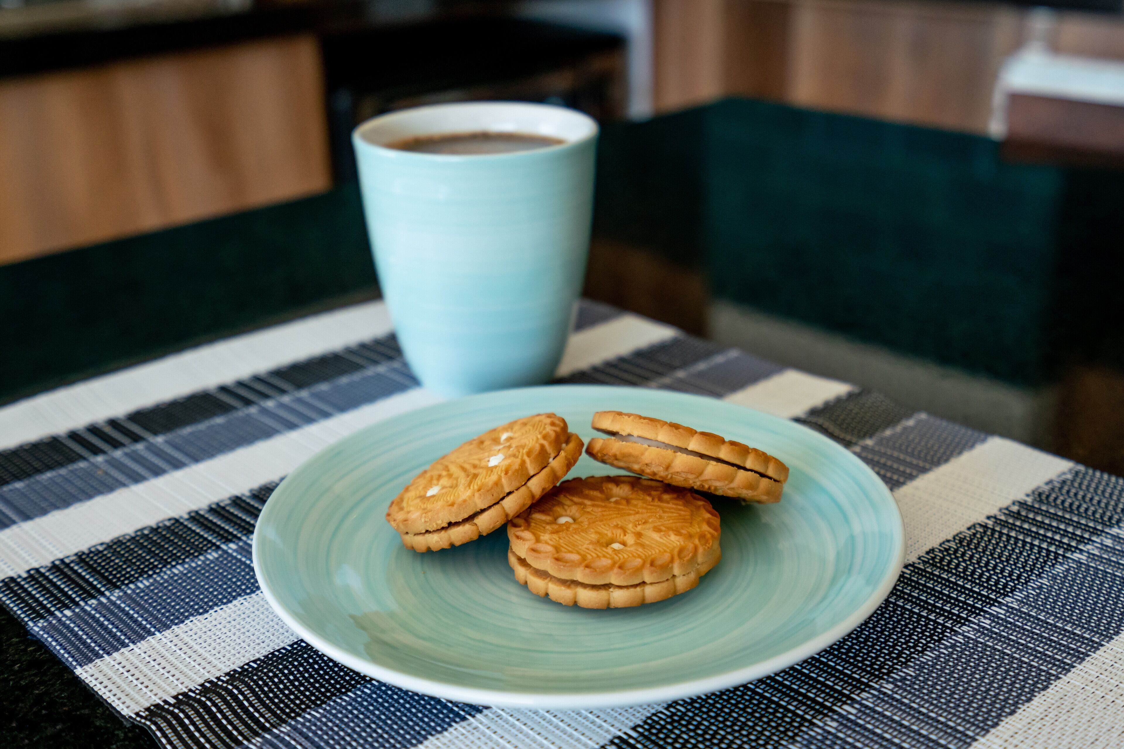 A plate of cookies on a blue plate, a blue cup, and a checkered tablecloth.