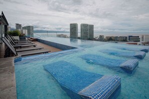 Una piscina infinita en la azotea con agua cristalina, rodeada de sillones de descanso y vistas a la ciudad.