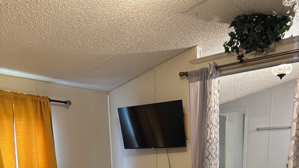Un dormitorio con cama, televisor y baño visible en un espejo, además de una cortina amarilla.