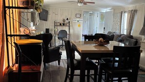 Una cocina moderna con suelo de madera oscura, un comedor con mesa y sillas de madera, un ventilador de techo y vistas al salón a través de una puerta abierta.