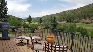 Una terraza con mobiliario exterior y una parrilla, con vista a un paisaje boscoso.