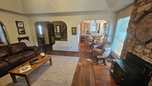 Una sala de estar con chimenea, sofá de cuero, mesa de centro de madera y un comedor al fondo.