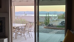 Un patio con mesa y sillas, un pozo de fuego y vistas a montañas y un cuerpo de agua.