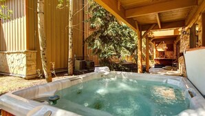 Un bain à remous situé dans un espace extérieur abrité, avec un mur en pierre et des poutres en bois.