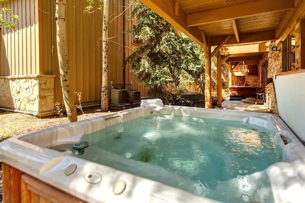 A hot tub in a covered outdoor area with a stone wall and wooden beams. - Abode at Black Bear #152, hot tub, pool & gym, Silver Lake village (Park City)