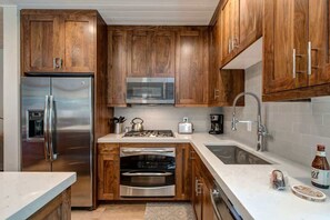 A kitchen with wooden cabinets, stainless steel appliances, a microwave, oven, and a sink.