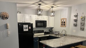 A modern kitchen with white cabinets, a black refrigerator, a microwave, and a granite countertop. There are three wooden stools and a fire extinguisher. - Attitash Mountain Resort Condo- 3 Floors, Sleeps 12- Story Land, Ski, Shop, Golf (Bartlett)