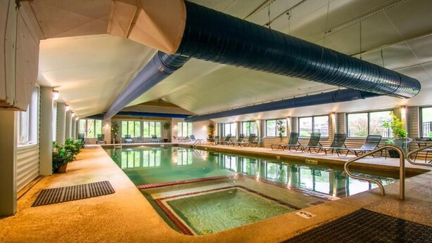 An indoor swimming pool with clear water, surrounded by lounge chairs and potted plants. - Attitash Mountain Resort Condo- 3 Floors, Sleeps 12- Story Land, Ski, Shop, Golf (Bartlett)