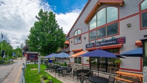 A restaurant with outdoor seating, including tables and umbrellas, and a sign indicating it serves lunch, dinner, and breakfast. - Attitash Mountain Resort Condo- 3 Floors, Sleeps 12- Story Land, Ski, Shop, Golf (Bartlett)