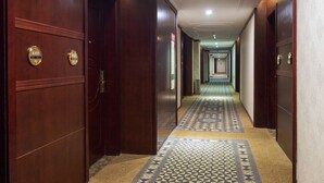 A hotel hallway with wooden doors, a patterned carpet, and a long corridor leading to a bright end. - Weiluola Hotel Xiamen (Xiamen)
