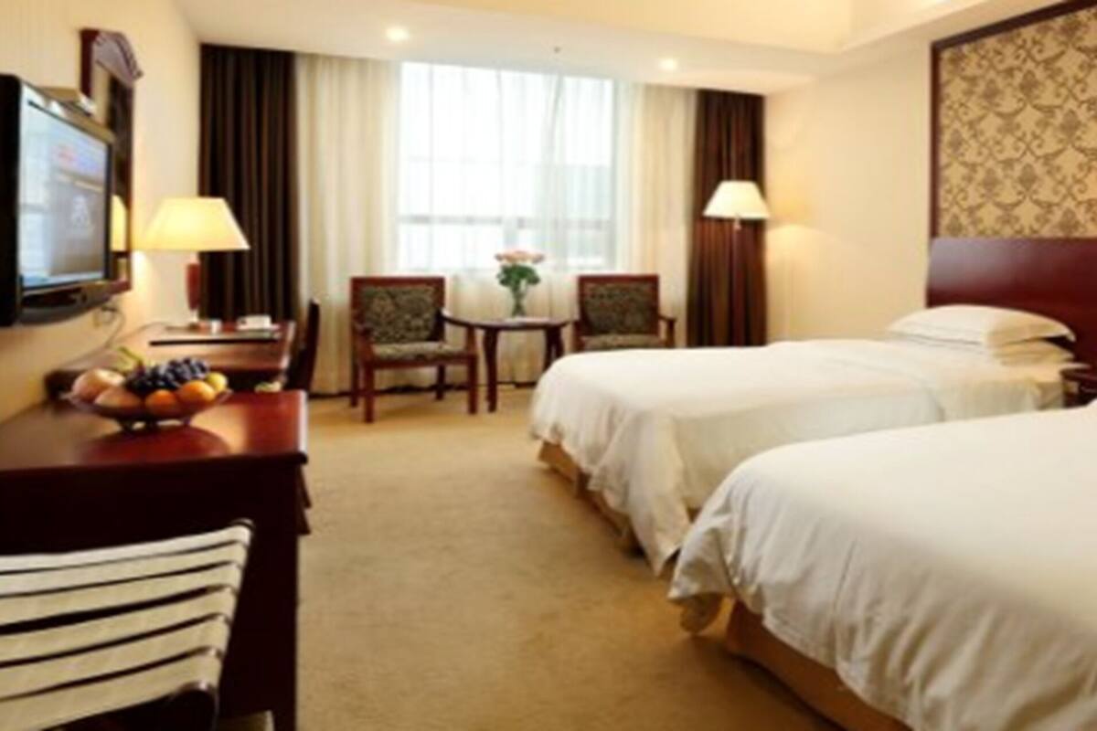 Ein Hotelzimmer mit zwei Betten, einem Schreibtisch mit Lampe, einem Fernseher und einem kleinen Tisch mit Obst.