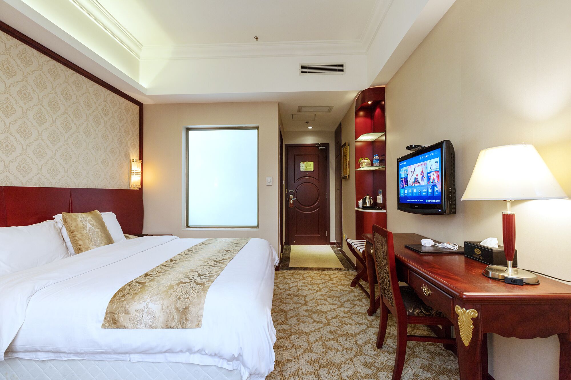 Une chambre d’hôtel avec un grand lit, un bureau avec un ordinateur, une télévision et une lampe.