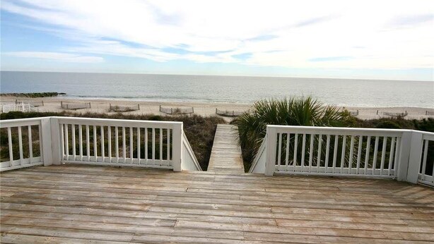Una terraza de madera que conduce a una playa, con barandilla blanca.