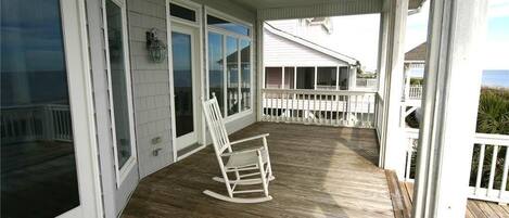 A covered porch with a rocking chair, white railings, and a view of the ocean.