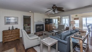 A spacious living room with a fireplace, a ceiling fan, and a view of the outdoors. - Beach Blessing- Whole House (Edisto Island)